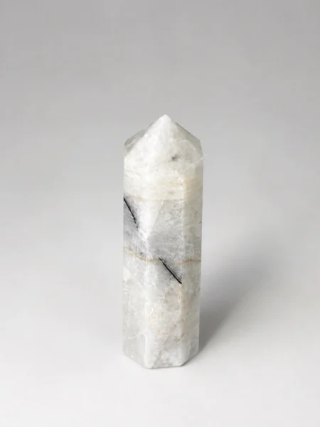 Side view of small Moonstone crystal tower showing creamy white colouring and a dark diagonal mineral inclusion